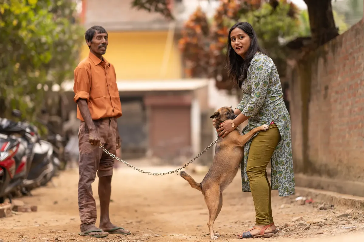 A man and woman outdoors bonding with a pet dog on a sunny urban street.